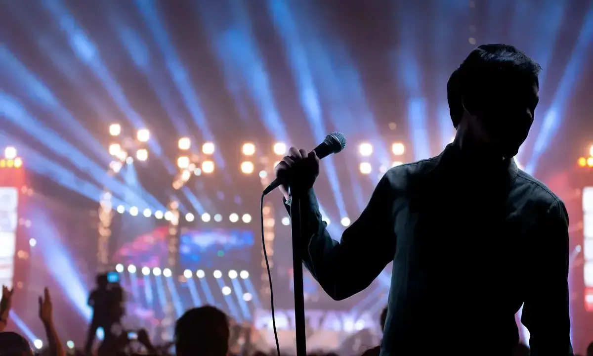 Cantante sul palco con microfono, luci sfocate e folla. Il **take on me significato** è l'essenza di un'esibizione che cattura l'anima.