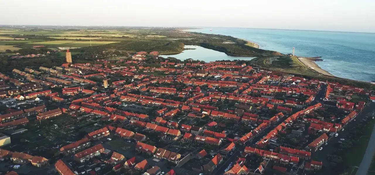 Luftaufnahme einer Küstenstadt in den Niederlanden mit roten Dächern, einem Leuchtturm und dem Meer. Drohnenaufnahmen zeigen die Schönheit der Niederlande.