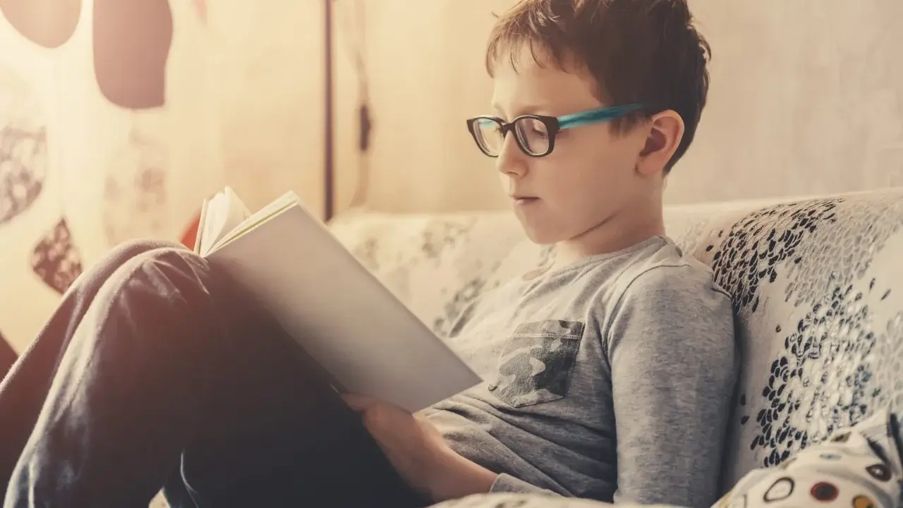 Bambino con occhiali legge un libro, concentrato su come imparare una poesia a memoria.