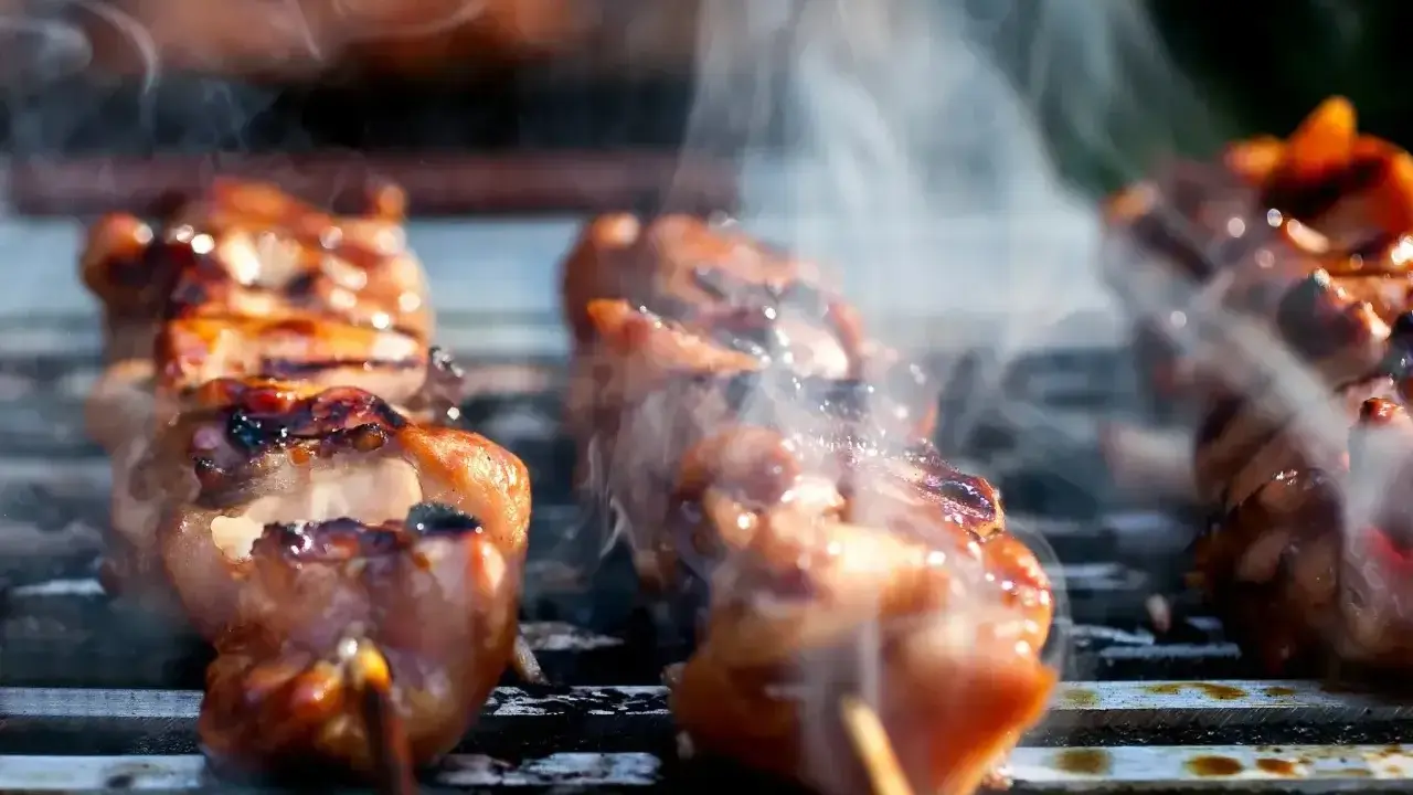 Aromatyczne yakitori skwierczy na grillu, otoczone kłębuszkami dymu.