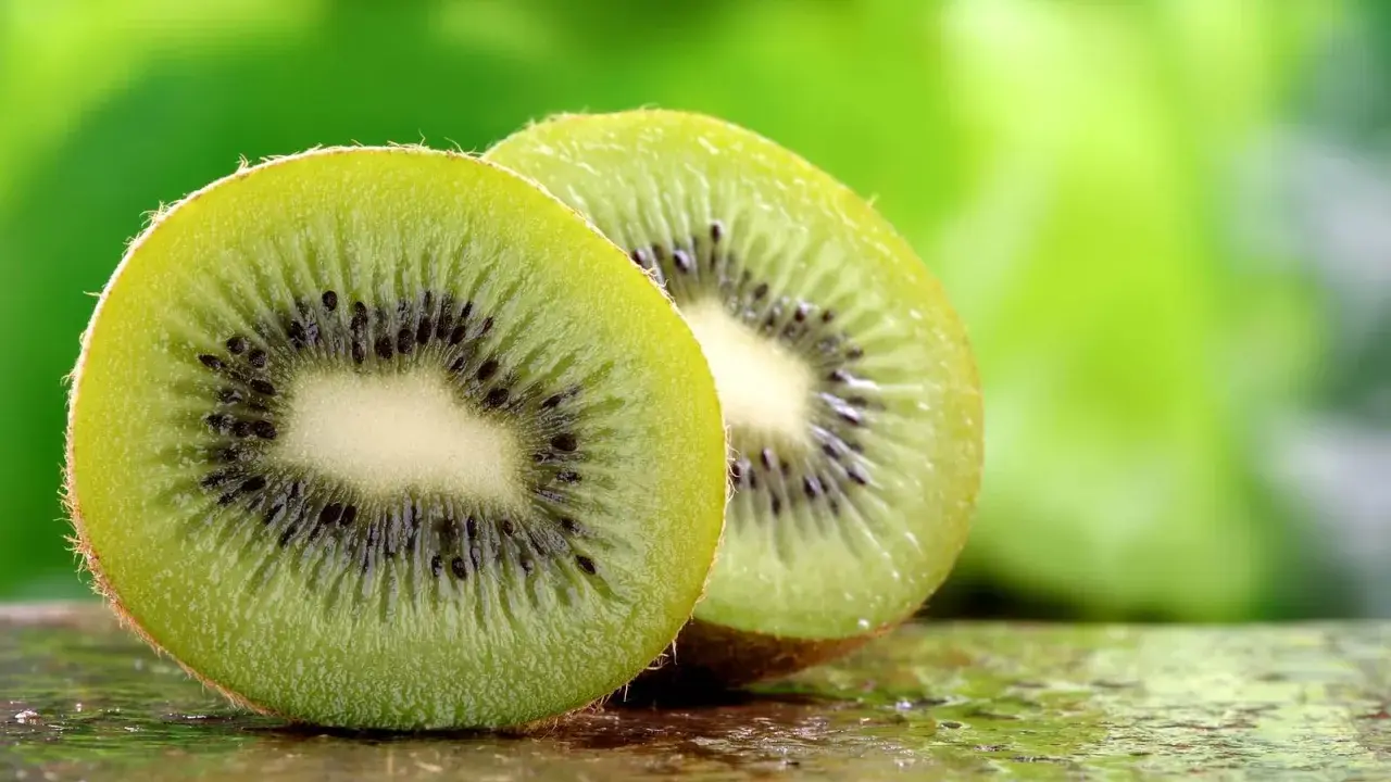 Dwa soczyste kiwi, przekrojone na pół, ukazują swoje zielone wnętrze z czarnymi pestkami. To naturalne kiwi co leczy, pełne witamin.