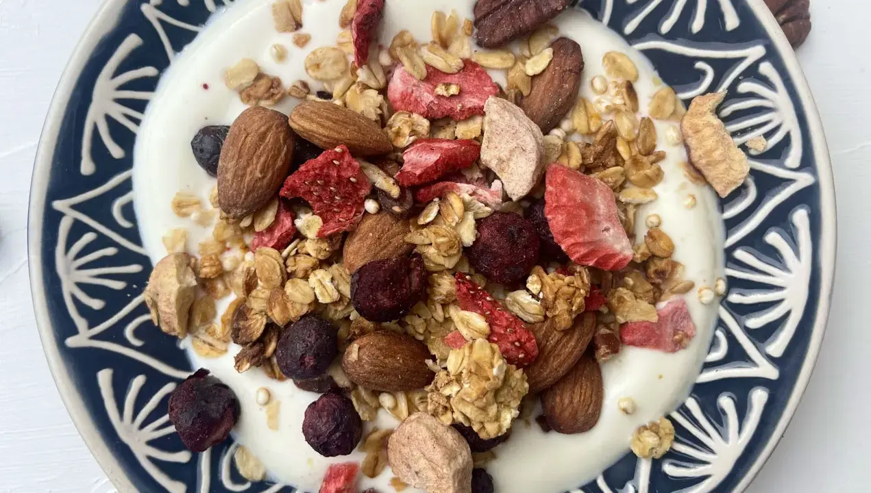 Schüssel mit Joghurt, garniert mit knusprigem Müsli, Mandeln, gefriergetrockneten Erdbeeren und Blaubeeren. Perfekt für gesunde Frühstücks-Granola-Rezepte.