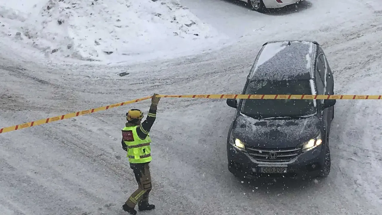 En räddningsarbetare spärrar av ett område med band. Snö faller och täcker marken och en bil. Kanske har något ruttnande material hittats.