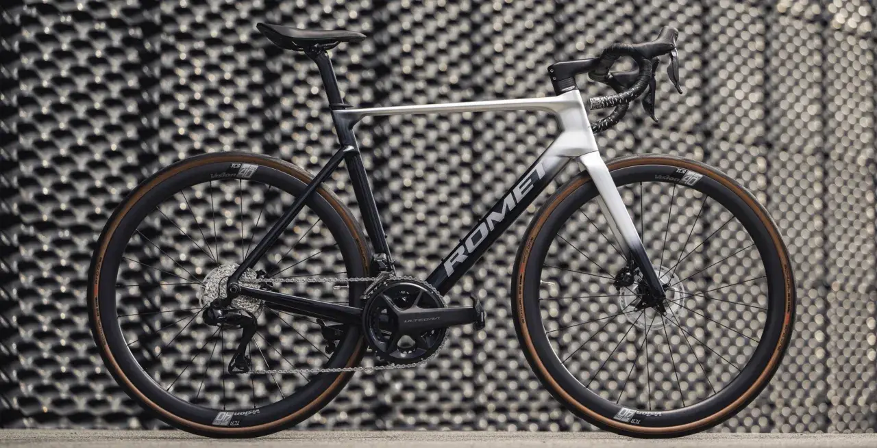 Nowoczesny rower szosowy marki Romet z osprzętem Shimano Ultegra, prezentujący się na tle geometrycznej ściany.