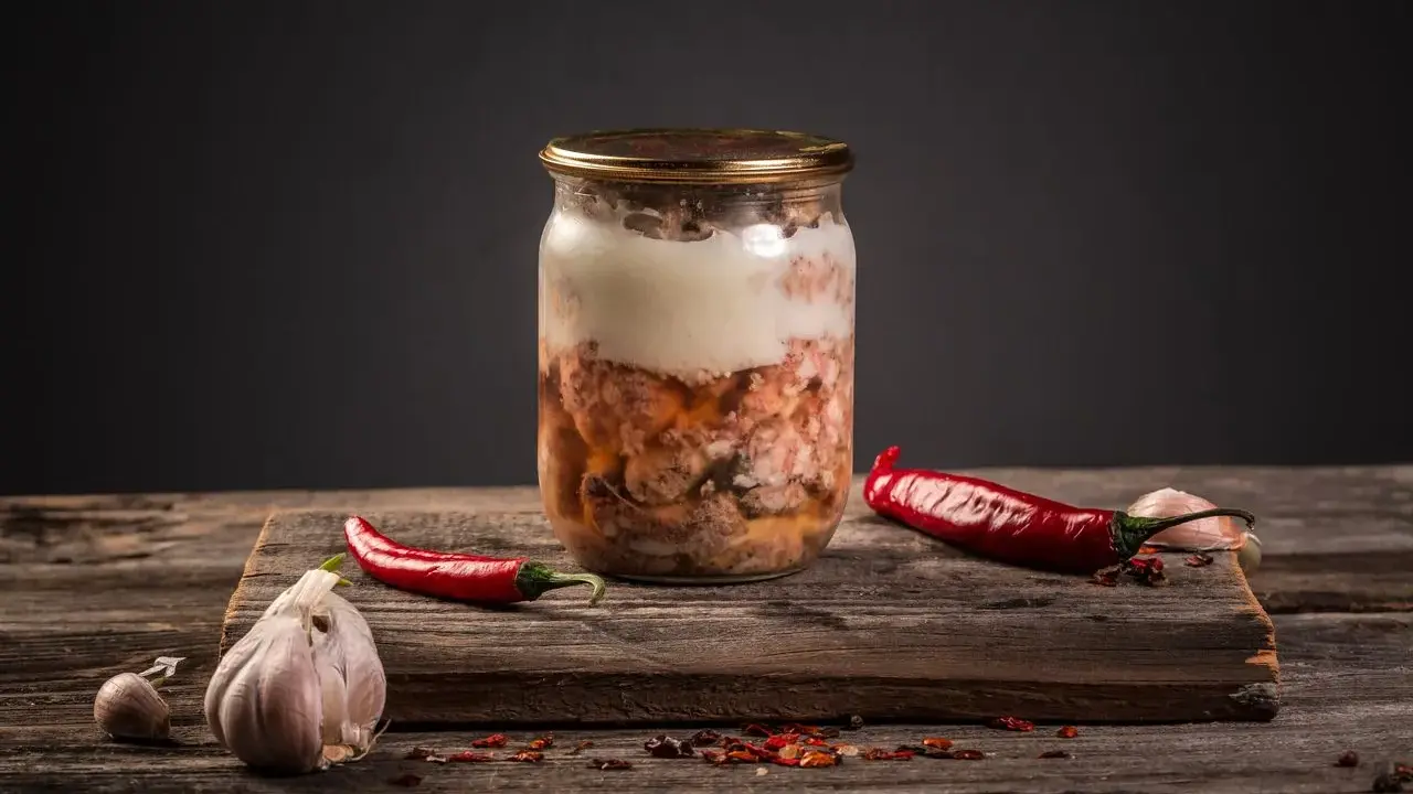 Słoik z mięsem, czosnek i papryczki chili. Przygotowanie tyndalizacji mięsa w piekarniku.