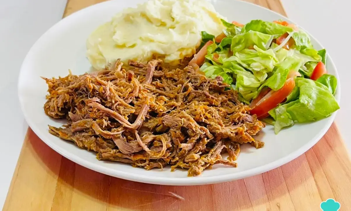 Plato de carne mechada jugosa, puré de papas cremoso y ensalada fresca de lechuga y tomate.