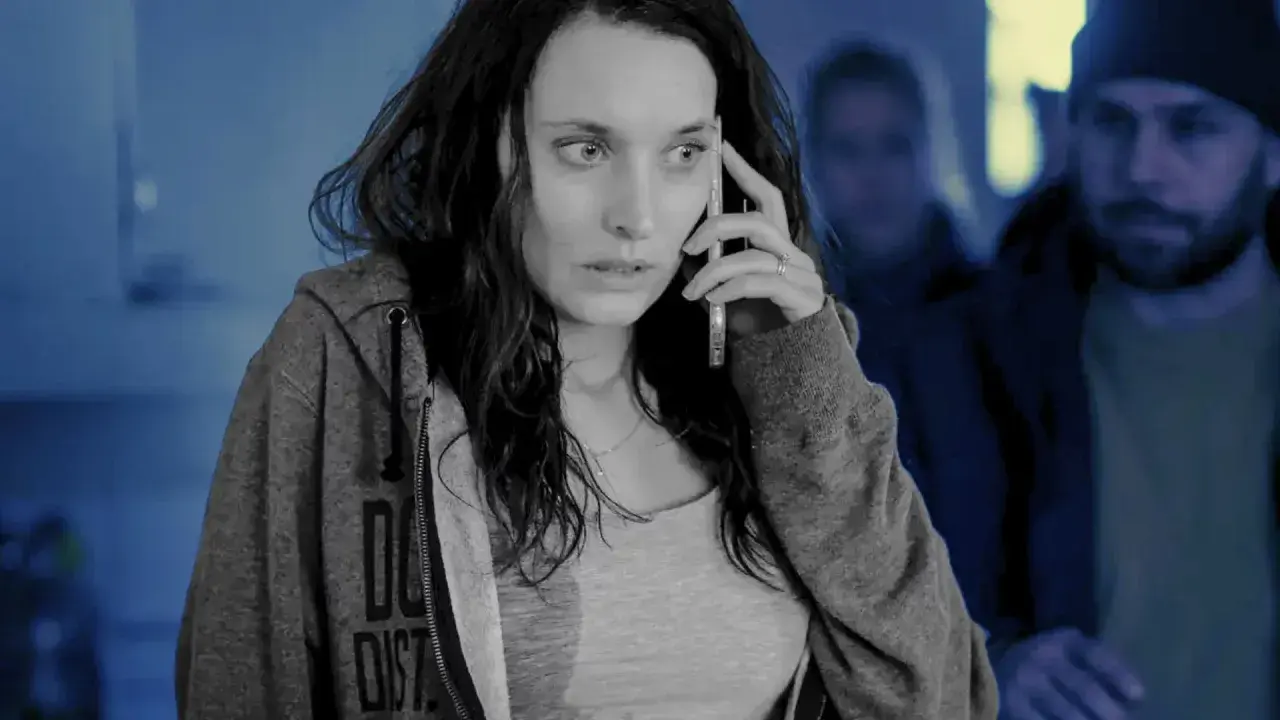 Przerażona kobieta rozmawia przez telefon, podczas gdy w tle widać zamazane postacie. Scena jak ze skandynawskich seriali kryminalnych.