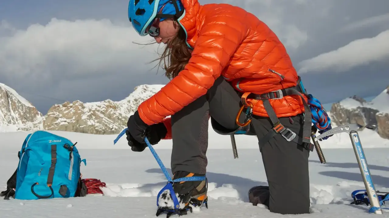 Alpinistka przygotowuje raki automatyczne lub półautomatyczne do wspinaczki. W tle góry.