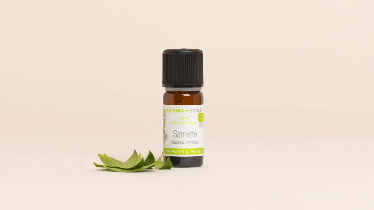 Flacon d'huile essentielle sarriette des montagnes, aux vertus purifiantes et toniques, accompagné de quelques feuilles fraîches.