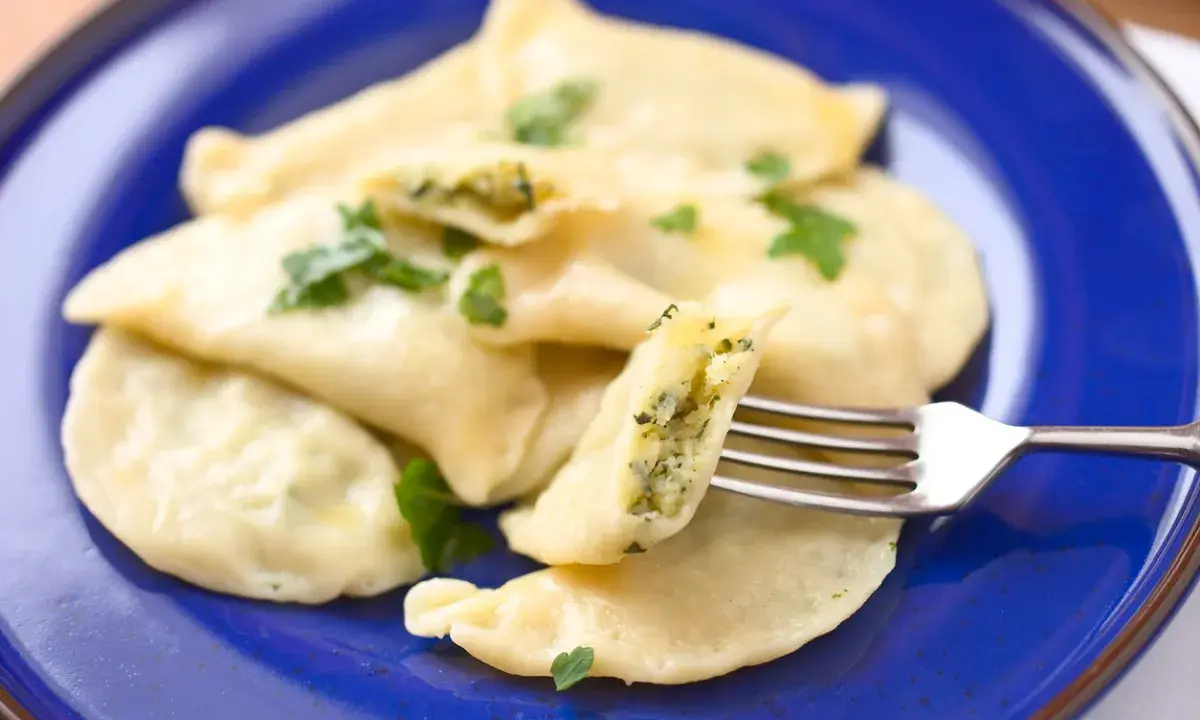 Pyszne pierogi ze szpinakiem i serem feta, udekorowane natką pietruszki, czekają na widelcu.
