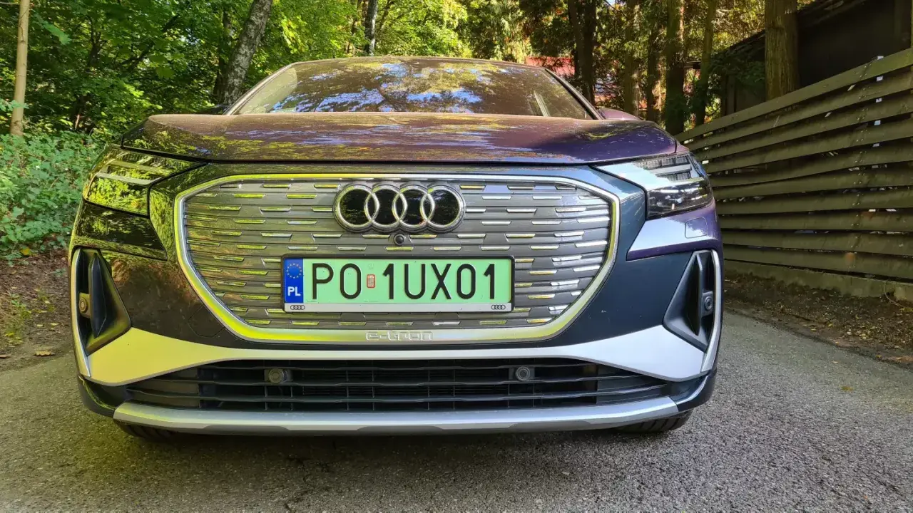 Elegancki, chromowany samochód Audi e-tron z polskimi tablicami rejestracyjnymi stoi na tle zielonego lasu.