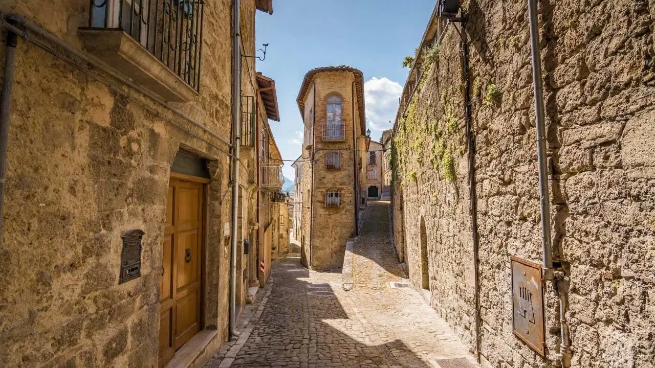 Antica scala di borgo in pietra, con case strette e un cielo azzurro.