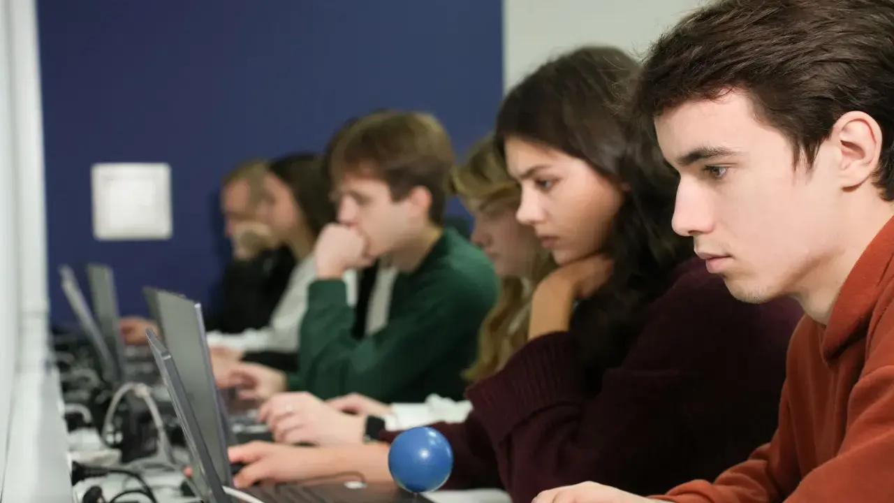 Studenci podczas zajęć z informatyki w Katowicach, skupieni na ekranach laptopów.