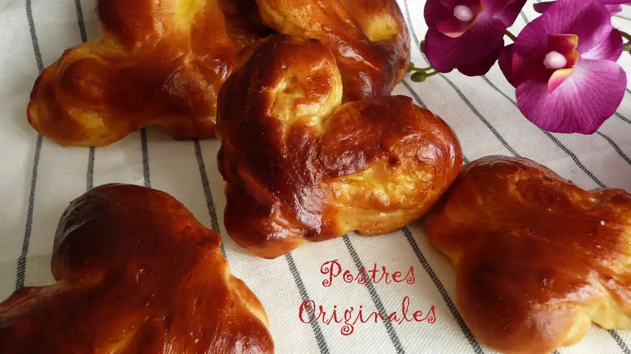 Pan de leche dorado y esponjoso, con forma de corazón, junto a orquídeas moradas. ¡Postres originales para disfrutar!