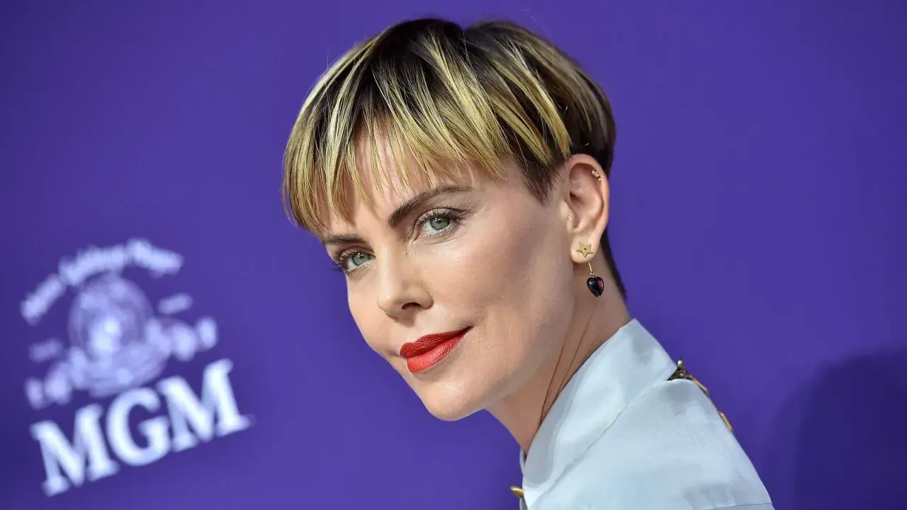 Charlize Theron mit fransigen Kurzhaarfrisuren Damen, rotem Lippenstift und Stern-Herz-Ohrringen vor MGM-Logo.