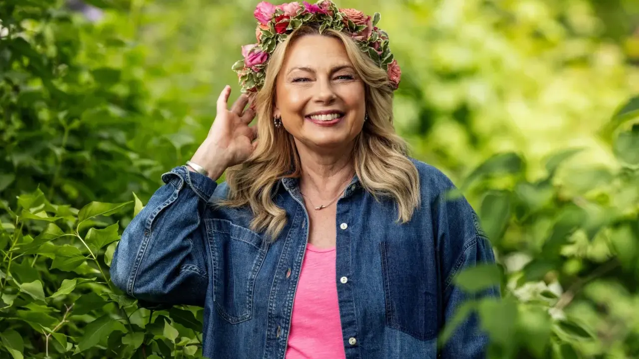 Glad kvinna med blomsterkrans ler i grönska. Hon är årets sommarpratare och bär jeansskjorta.