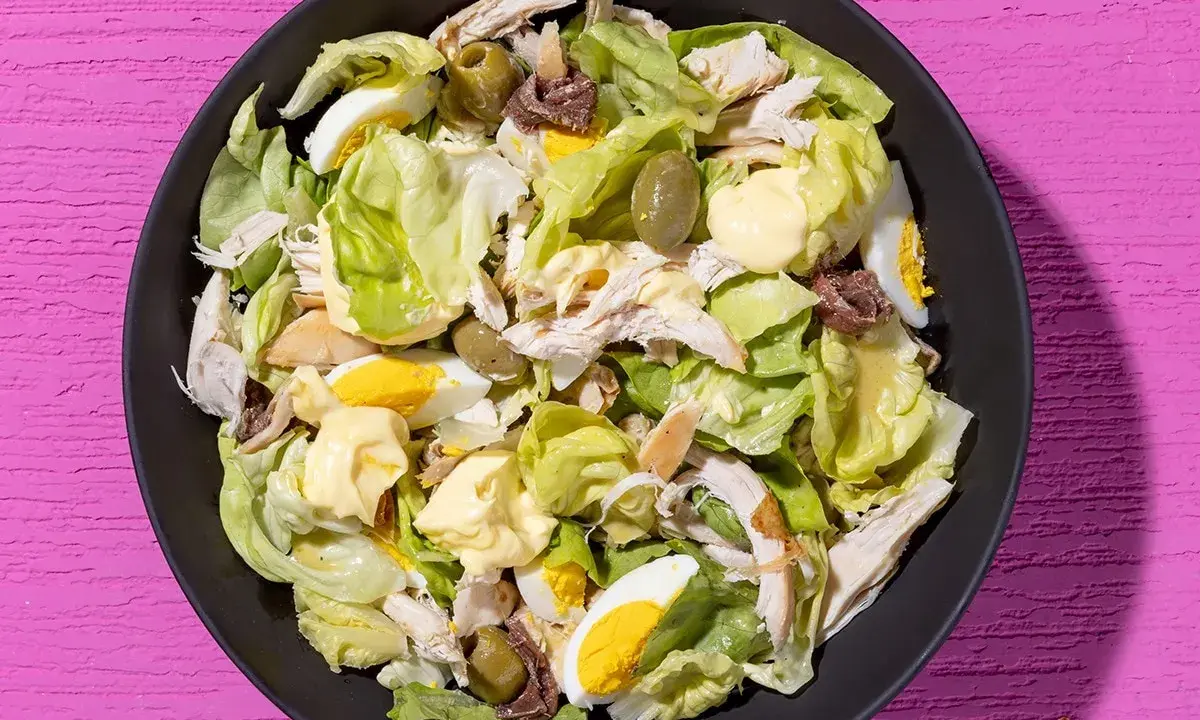 Insalata di pollo ricca con lattuga, uova sode, olive verdi e acciughe, condita con maionese.