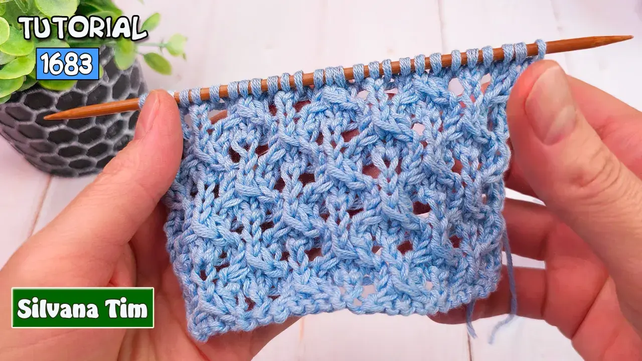 Manos tejiendo un patrón de puntos calados a dos agujas utilisima en hilo azul claro. El tejido muestra un diseño intrincado con agujeros y trenzas.