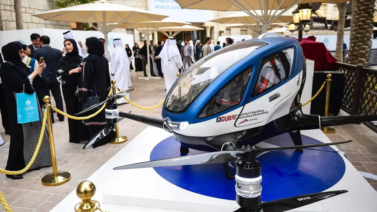 Ein futuristisches Flugtaxi, ein Dubai Drohne, steht auf einer Ausstellungsplattform. Menschen in traditioneller Kleidung betrachten das Gefährt.