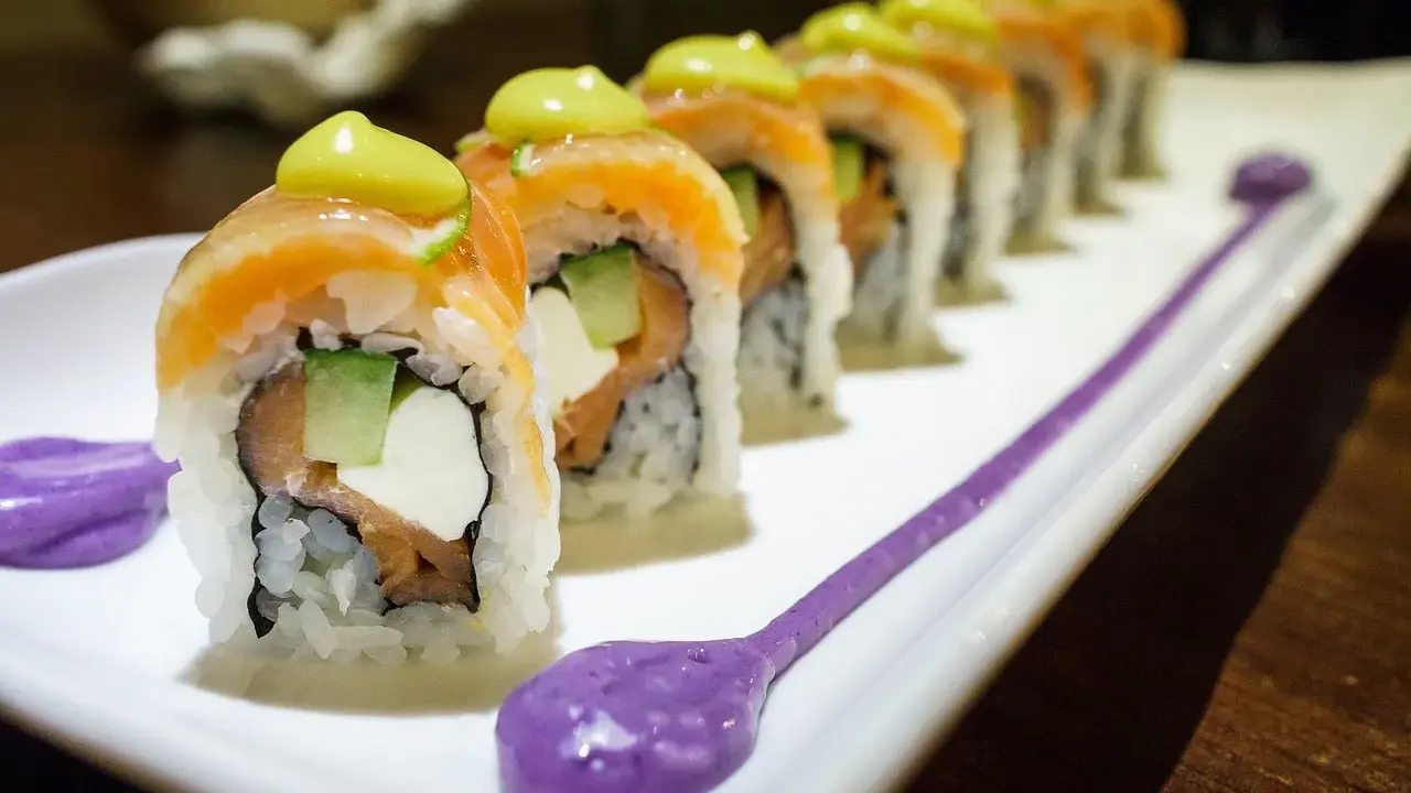 Une délicieuse recette maki original : rouleaux de saumon, avocat, concombre et fromage frais, ornés d'une touche de sauce verte et de purée violette.