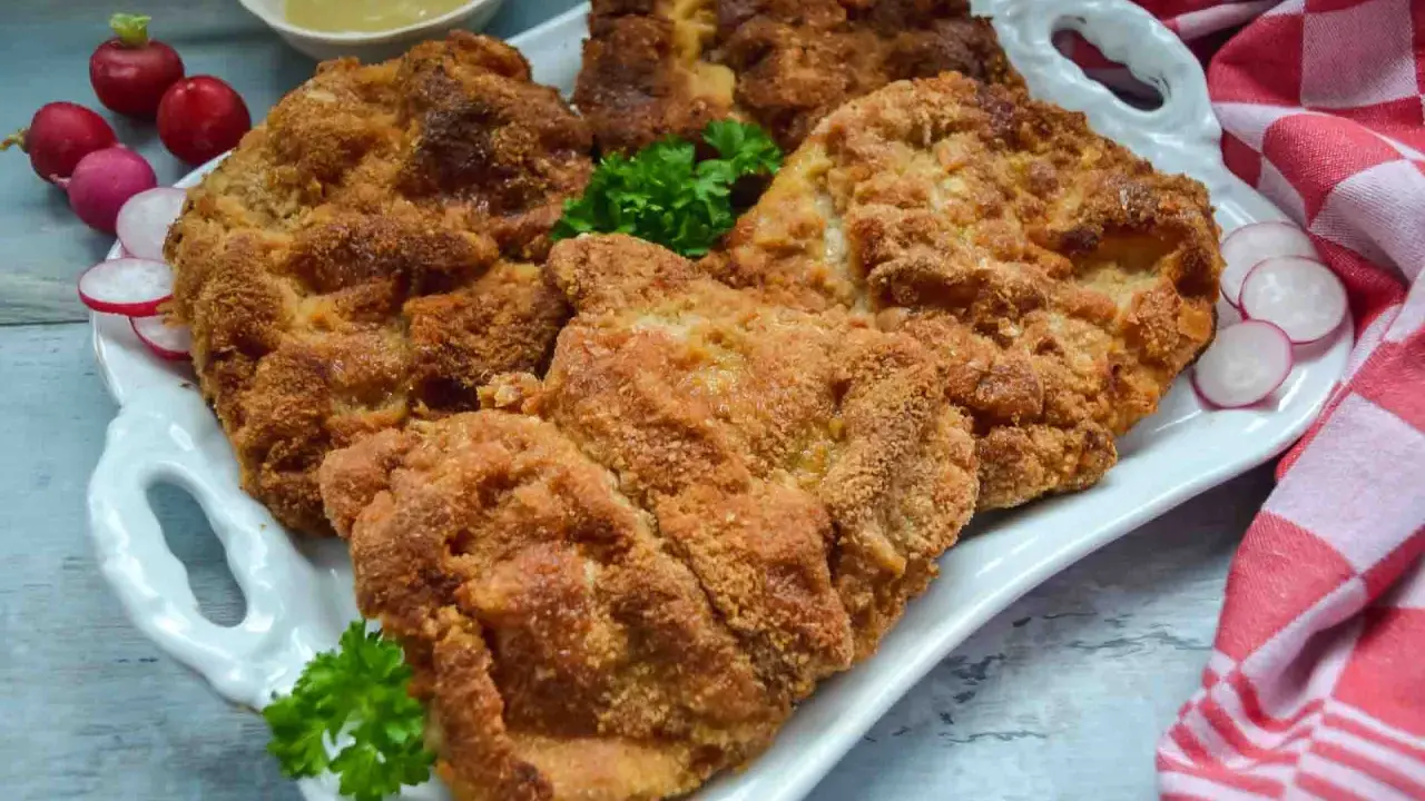Goldbraun paniertes Schnitzel, perfekt zubereitet, liegt auf einem weißen Teller, garniert mit Petersilie und Radieschen.