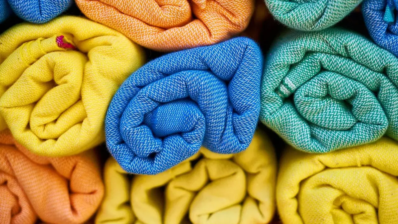 Rolled towels in vibrant colors: yellow, orange, blue, and green. These are made from biodegradable fabric, perfect for eco-conscious living.
