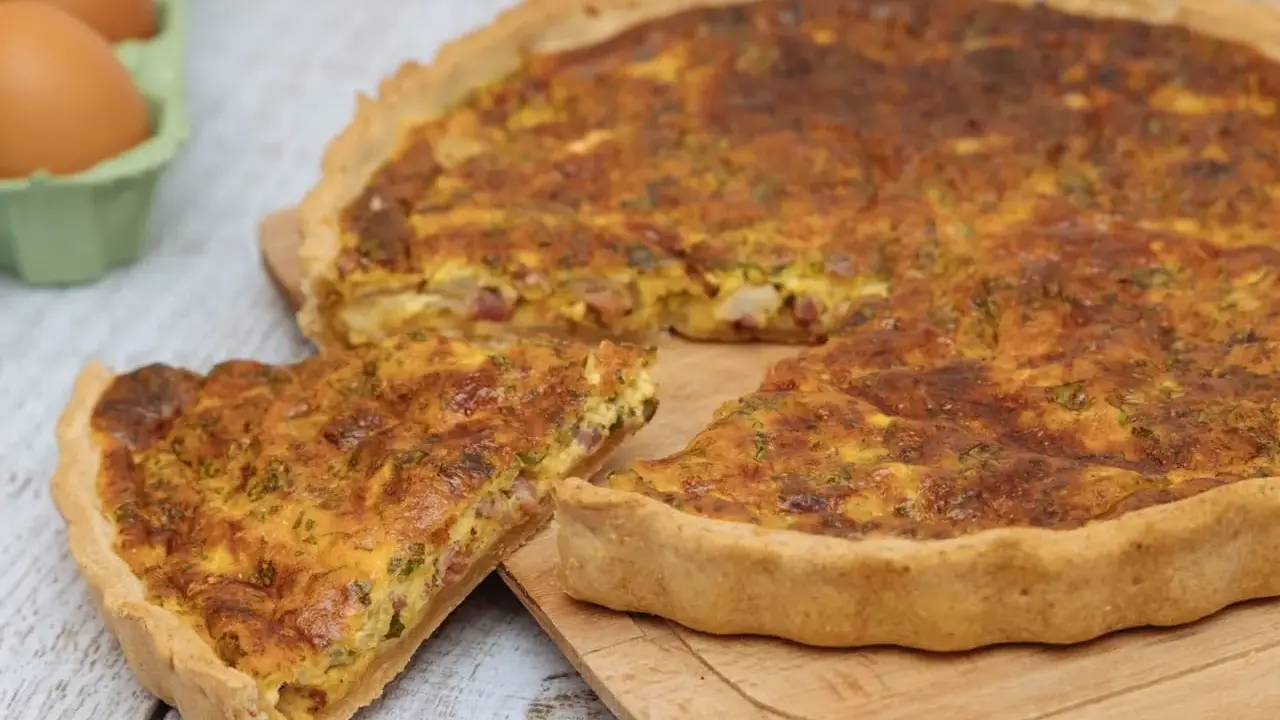 Une part de quiche lorraine dorée, avec sa garniture aux lardons et herbes, prête à être dégustée. La vraie recette quiche lorraine.
