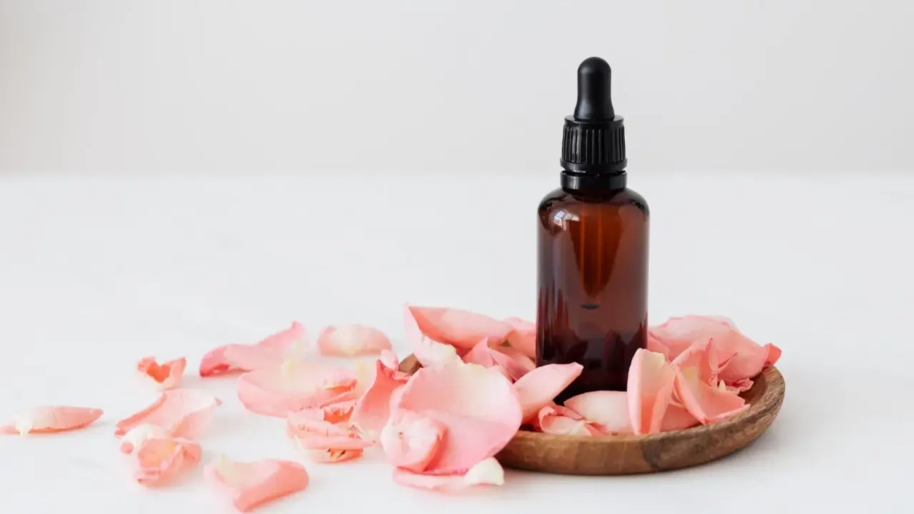 Flacon d'huile essentielle ambré entouré de pétales de rose. Un soin doux pour une femme enceinte.