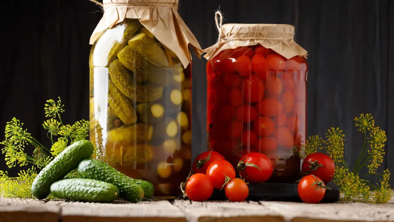 Deux bocaux de conserves, l'un de cornichons, l'autre de tomates, évoquent la culture du cornichon et des produits du jardin.