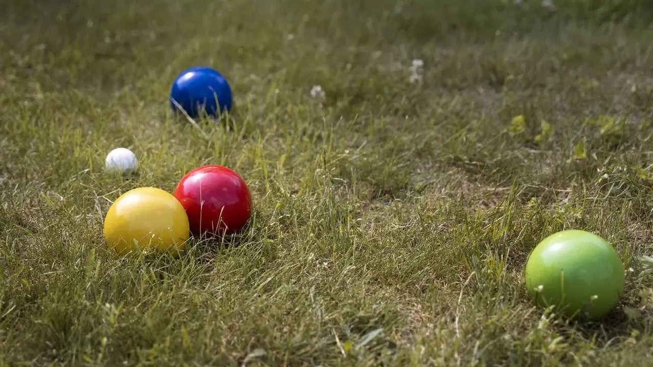 Boules colorées (jaune, rouge, bleu, vert) et une petite blanche sur l'herbe, prêtes pour un concours de pétanque.