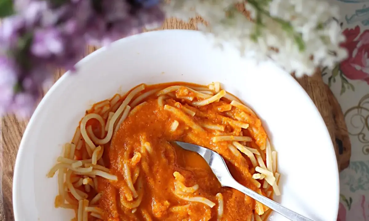 Pyszny przepis na sos do spaghetti, podany z makaronem w białej misce. W tle kwitnące kwiaty.
