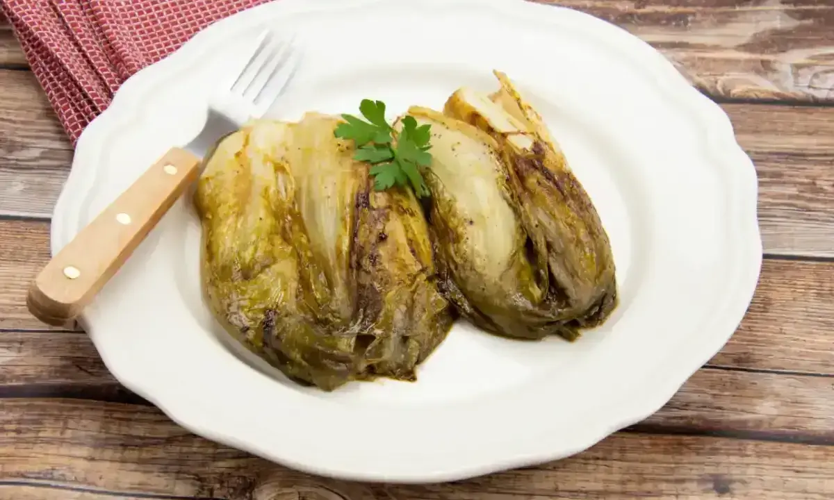 Deux endives caramélisées à la poêle, garnies de persil, sur une assiette blanche avec une serviette à carreaux rouges et une fourchette.