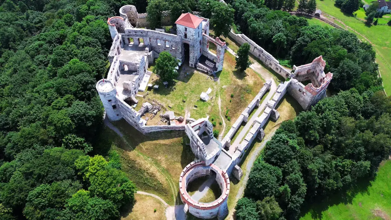 Zamek Rudno, otoczony bujną zielenią, prezentuje się jako malownicza ruina z kamiennymi murami i wieżami.