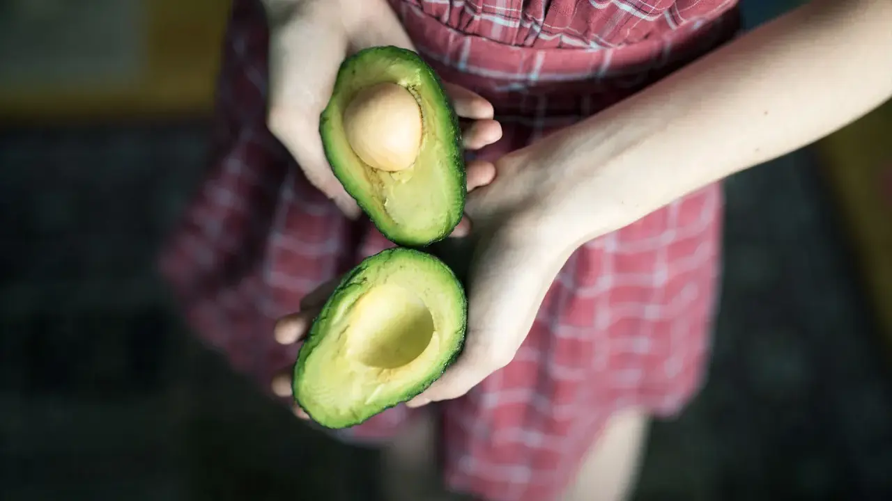 Hände halten eine aufgeschnittene Avocado, bereit für eine pflegende Avocado-Maske für die Haare.