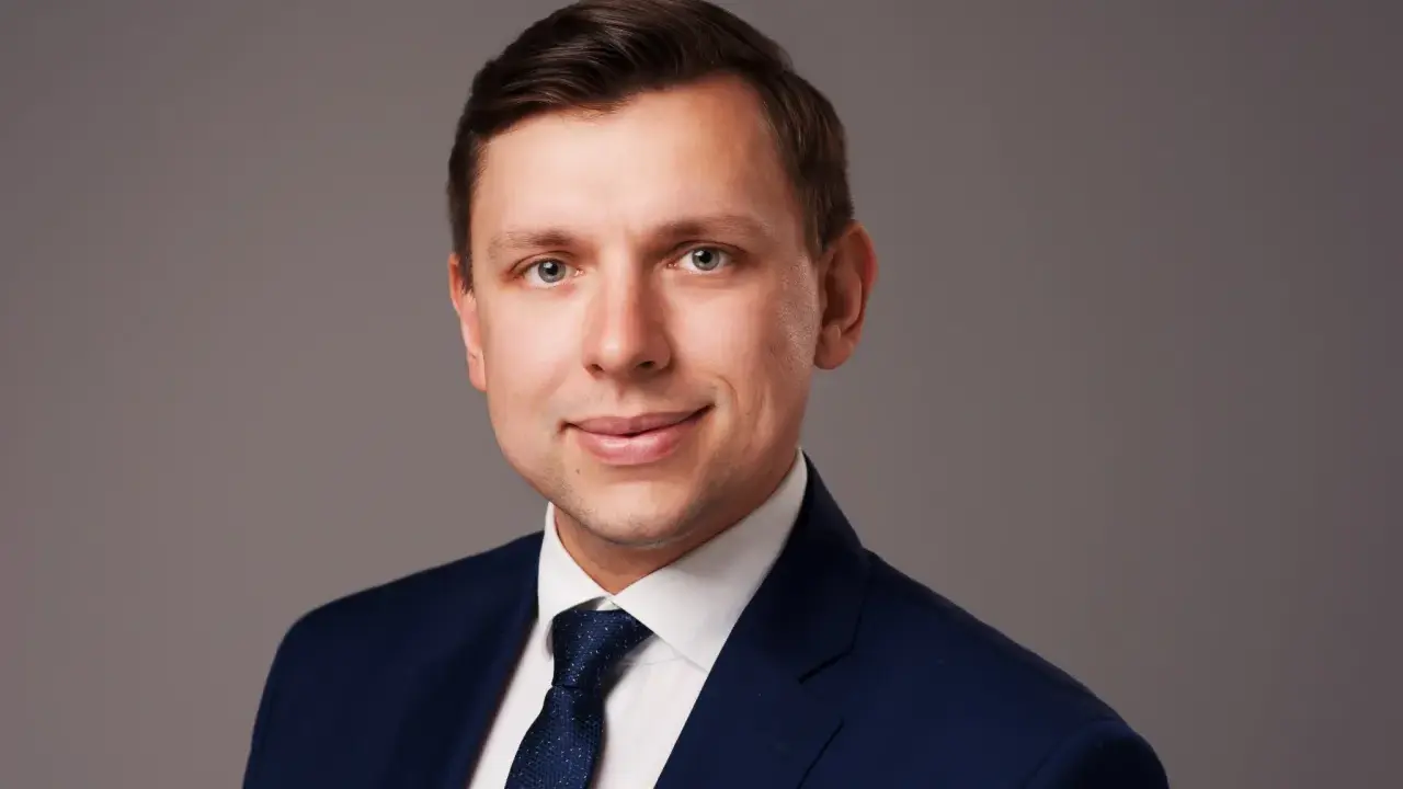 Portret mężczyzny w granatowym garniturze i białej koszuli z krawatem.