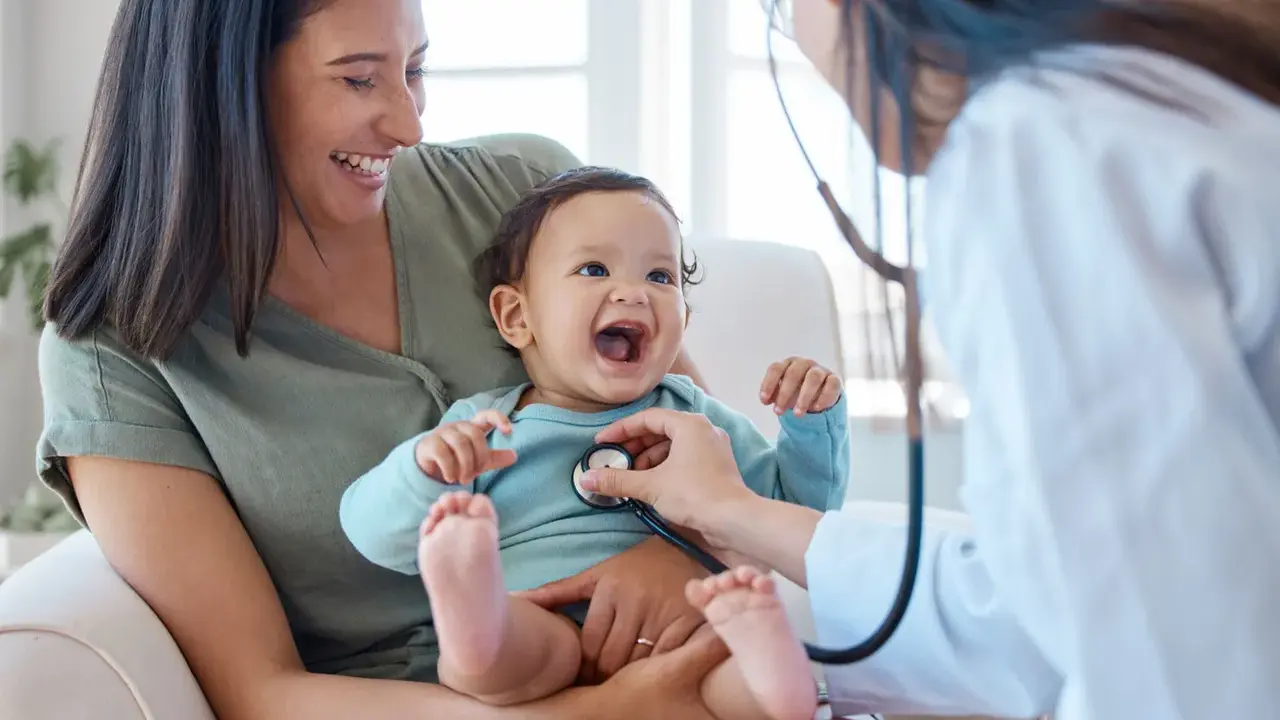 Glad mamma ser sitt barn få ett års vaccin. Läkaren lyssnar på barnets hjärta med stetoskop.