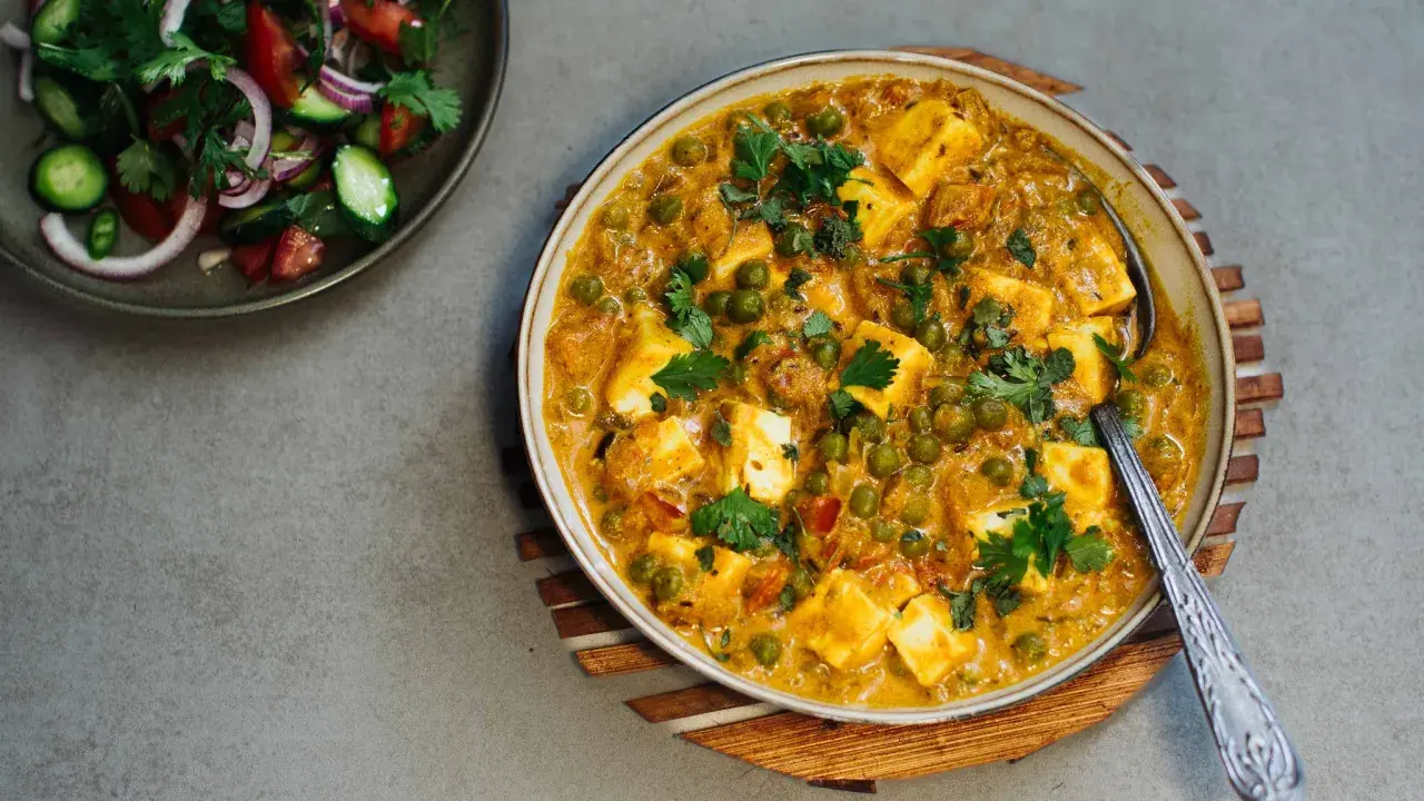 Cremiges Matar Paneer mit Erbsen und würzigen Paneer-Würfeln, garniert mit Koriander. Daneben ein frischer Salat.