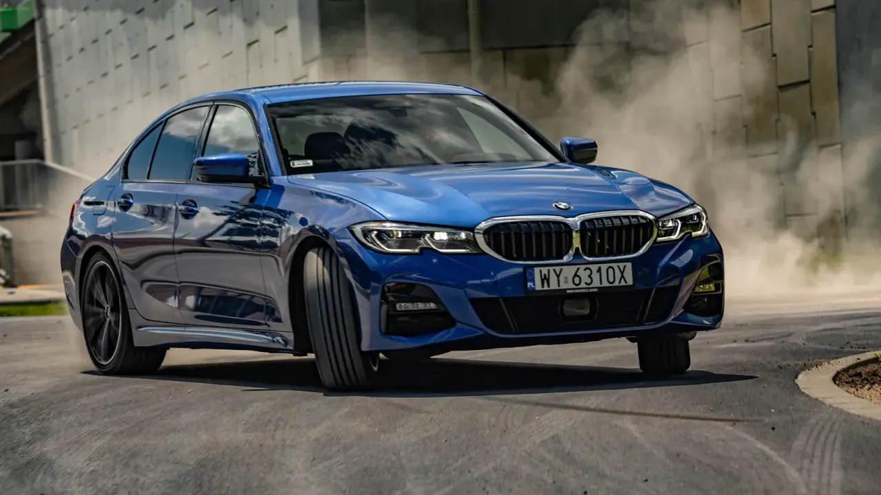 Niebieskie BMW 320i w zakręcie, unosząc tumany kurzu. Dynamiczna jazda na torze.