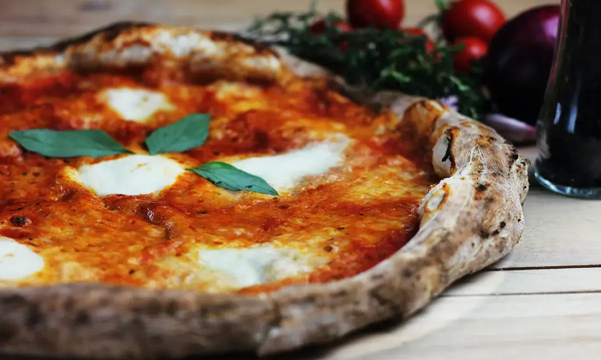 En perfekt pizza på grillen, med smält mozzarella och färsk basilika. Tomater och vitlök i bakgrunden.