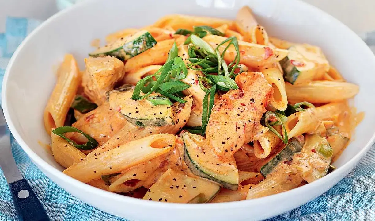 En skål med krämig penne med kyckling och zucchini, toppad med salladslök. En riktigt god pasta!