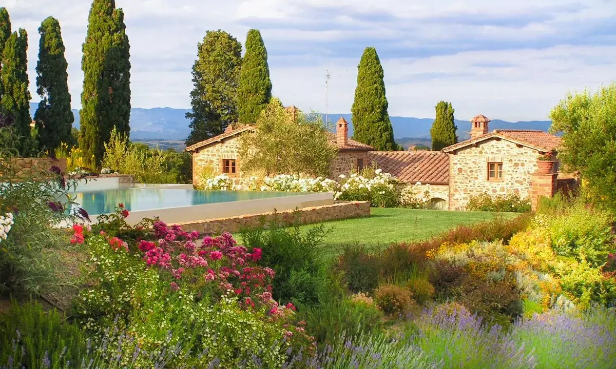 Vacanze in Toscana dove andare? Un casale in pietra con piscina, circondato da cipressi e un giardino fiorito.