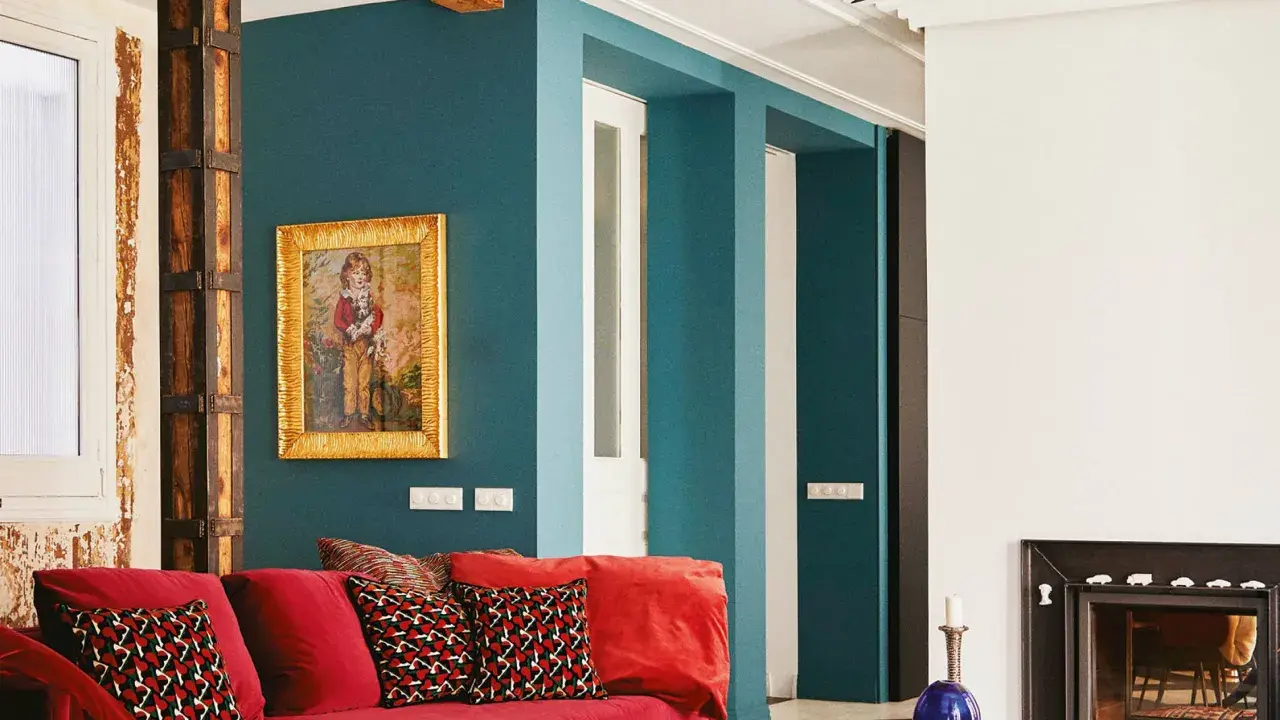 Sofá rojo vibrante con cojines estampados, pared azul petróleo y detalles rústicos. ¡Los mejores colores para pintar una casa!