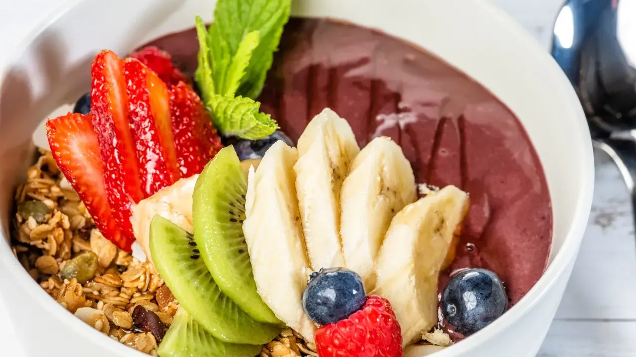 Acai-Schüssel mit Früchten, Granola und einem Hauch von Vitamin C. Erdbeeren, Bananen, Kiwi, Blaubeeren und Himbeeren machen diese Schüssel zu einem gesunden Genuss.