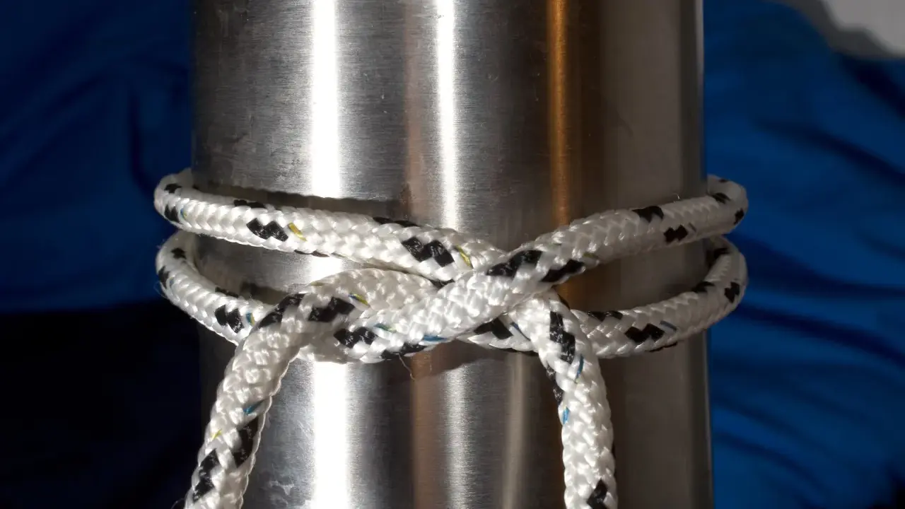 Un nœud pare battage, simple et efficace, sécurise une corde blanche et noire autour d'un mât métallique.