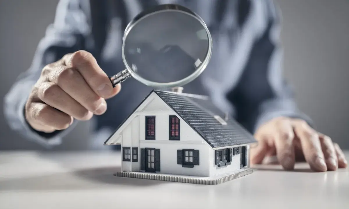 Une main examine une maquette de maison avec une loupe, symbolisant l'analyse pour un crédit construction maison.