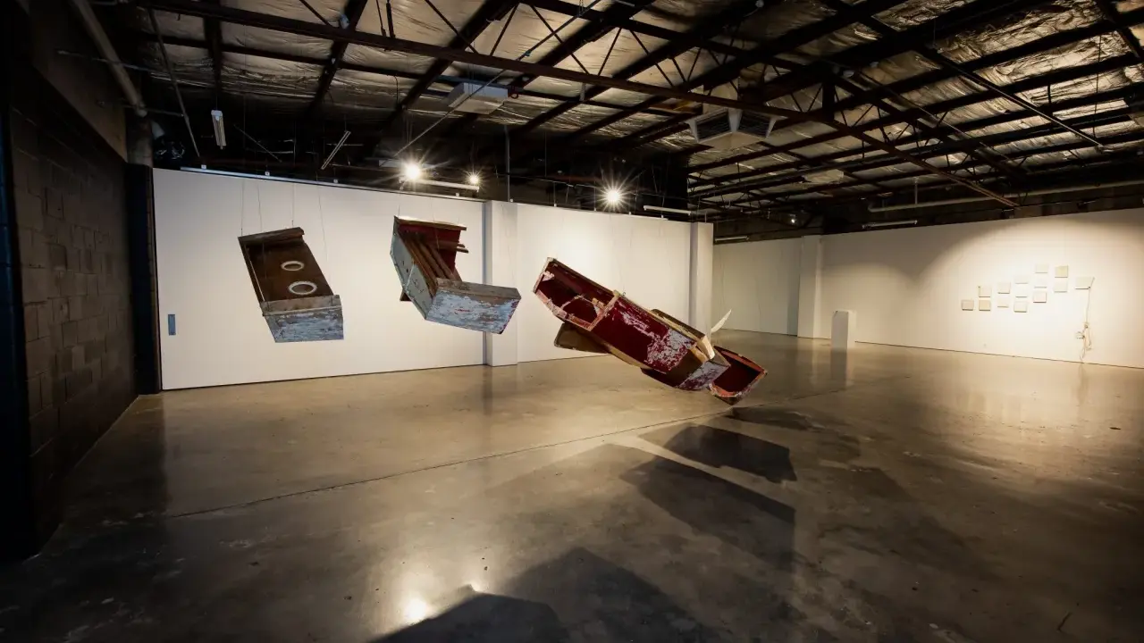 Suspended sculptures of weathered wood and metal hang in the spacious praxis gallery, casting long shadows on the concrete floor.