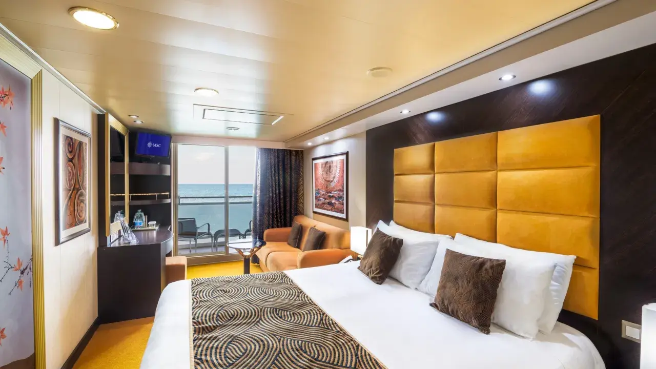 Interno di una cabina con balcone MSC Splendida: letto king-size, divano arancione, TV e vista mare.