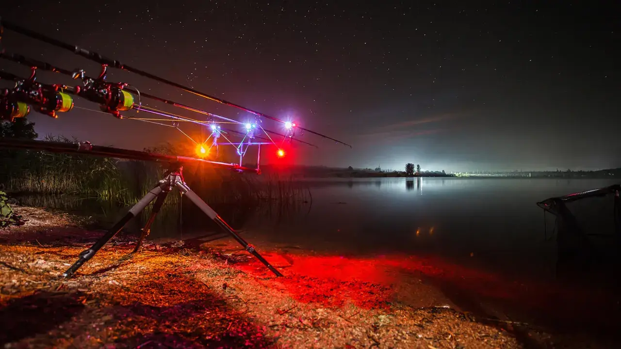Nocne łowienie karpi. Wędki na podpórce z sygnalizatorami brań, jezioro i gwiazdy. To jak zrobić świetlik na ryby.