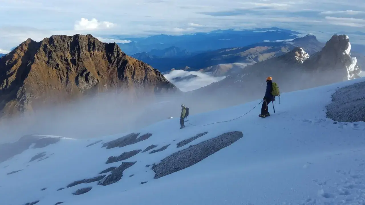 Dwóch alpinistów na ośnieżonym zboczu, w tle majestatyczne góry Ekwadoru, w tym najwyższy szczyt ekwadoru.
