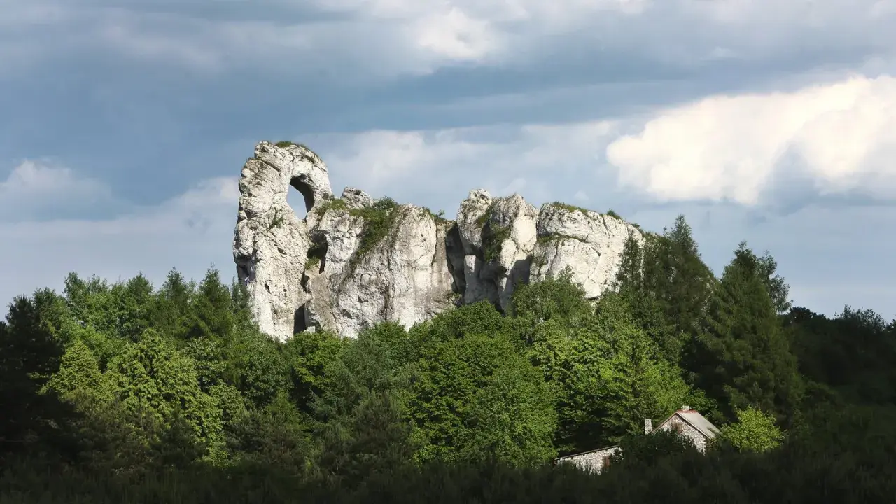 Imponujący okiennik wielki, skalna brama wśród zieleni, z ukrytą chatką.
